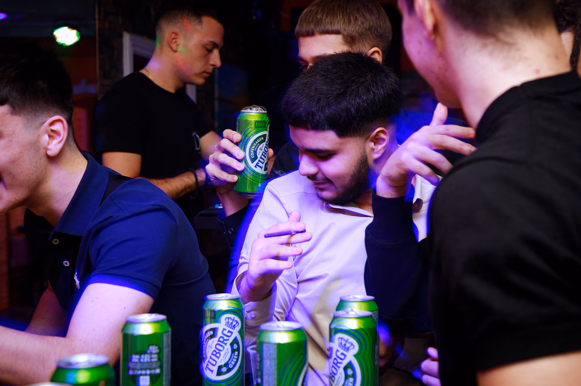 Grupa mladića na žurci drže limenke piva Tuborg i razgovaraju.