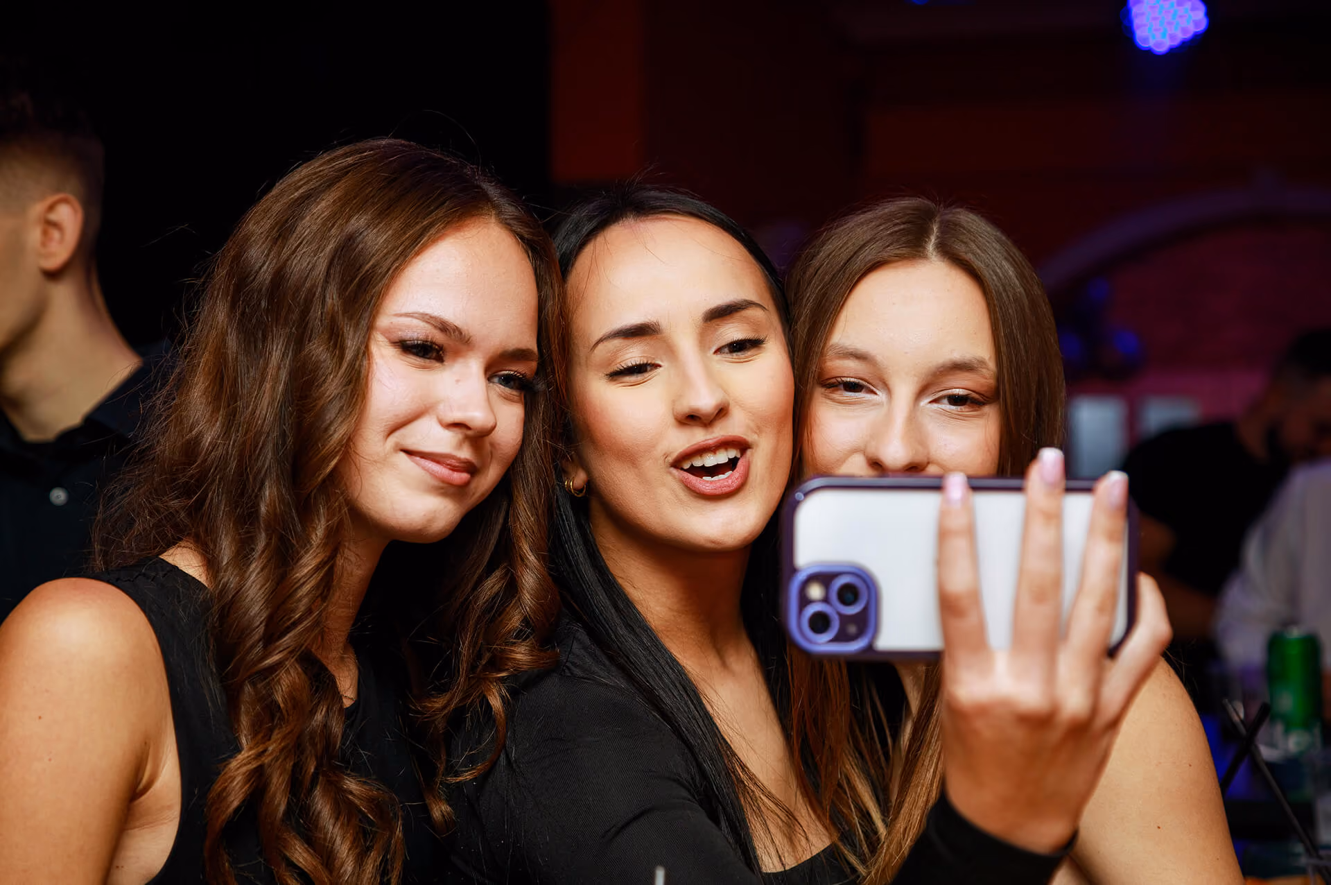 Tri žene nasmejane prave selfi u noćnom klubu.