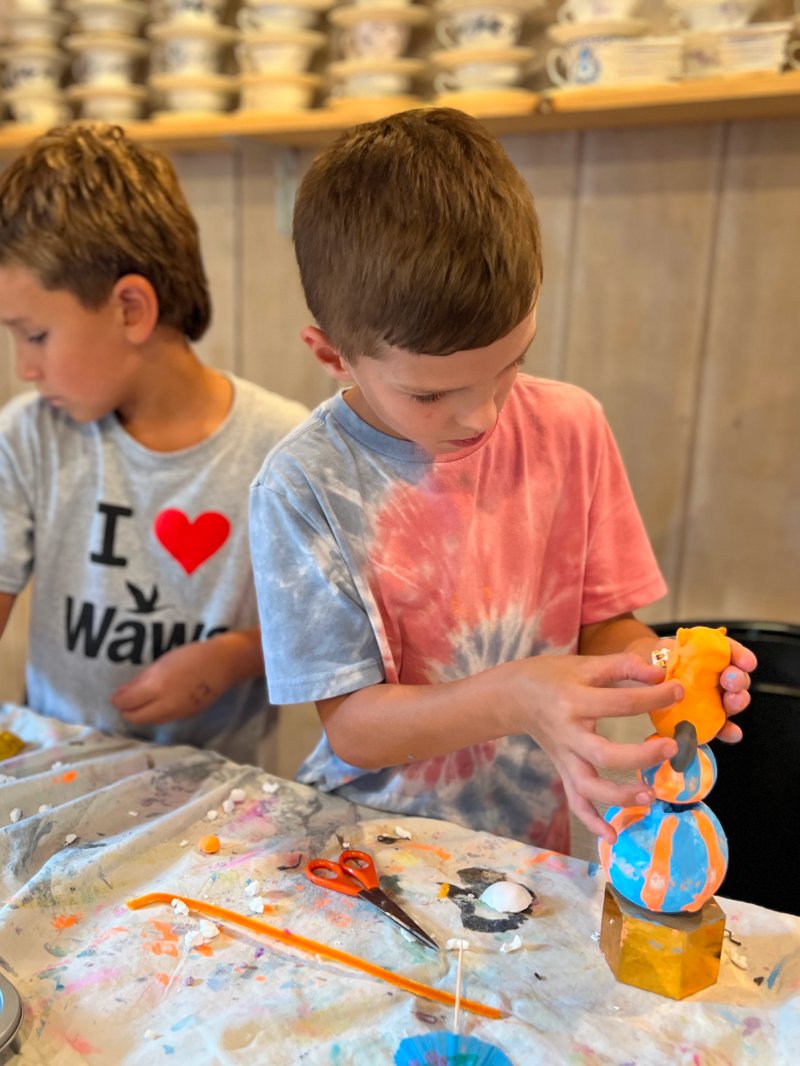 A boy works on his orange and blue clay sculpture