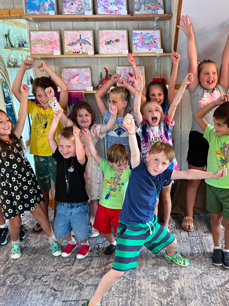 A collection of ArtStrong kids proudly celebrating their artwork behind them.