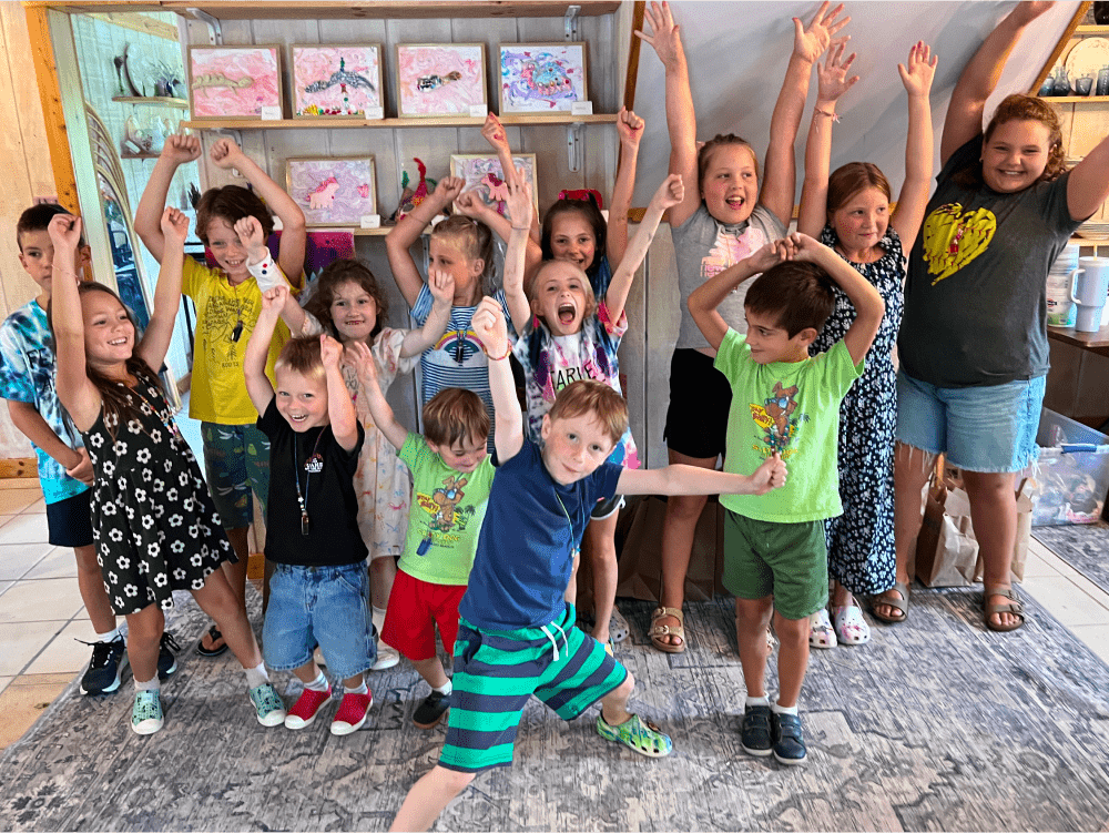 A collection of ArtStrong kids proudly celebrating their artwork behind them.