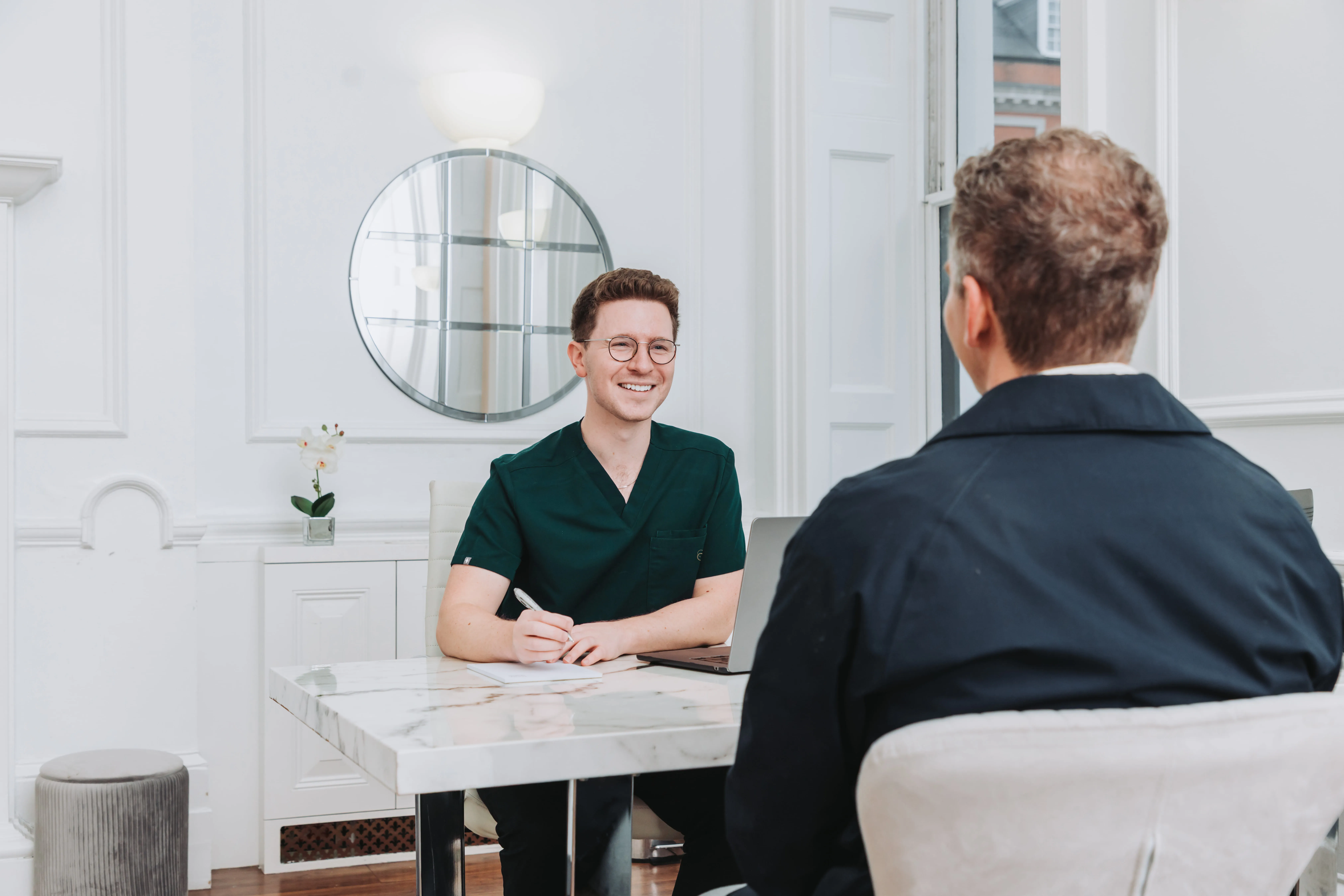 Smiling male healthcare professional in green scrubs consulting with a patient in a bright office.