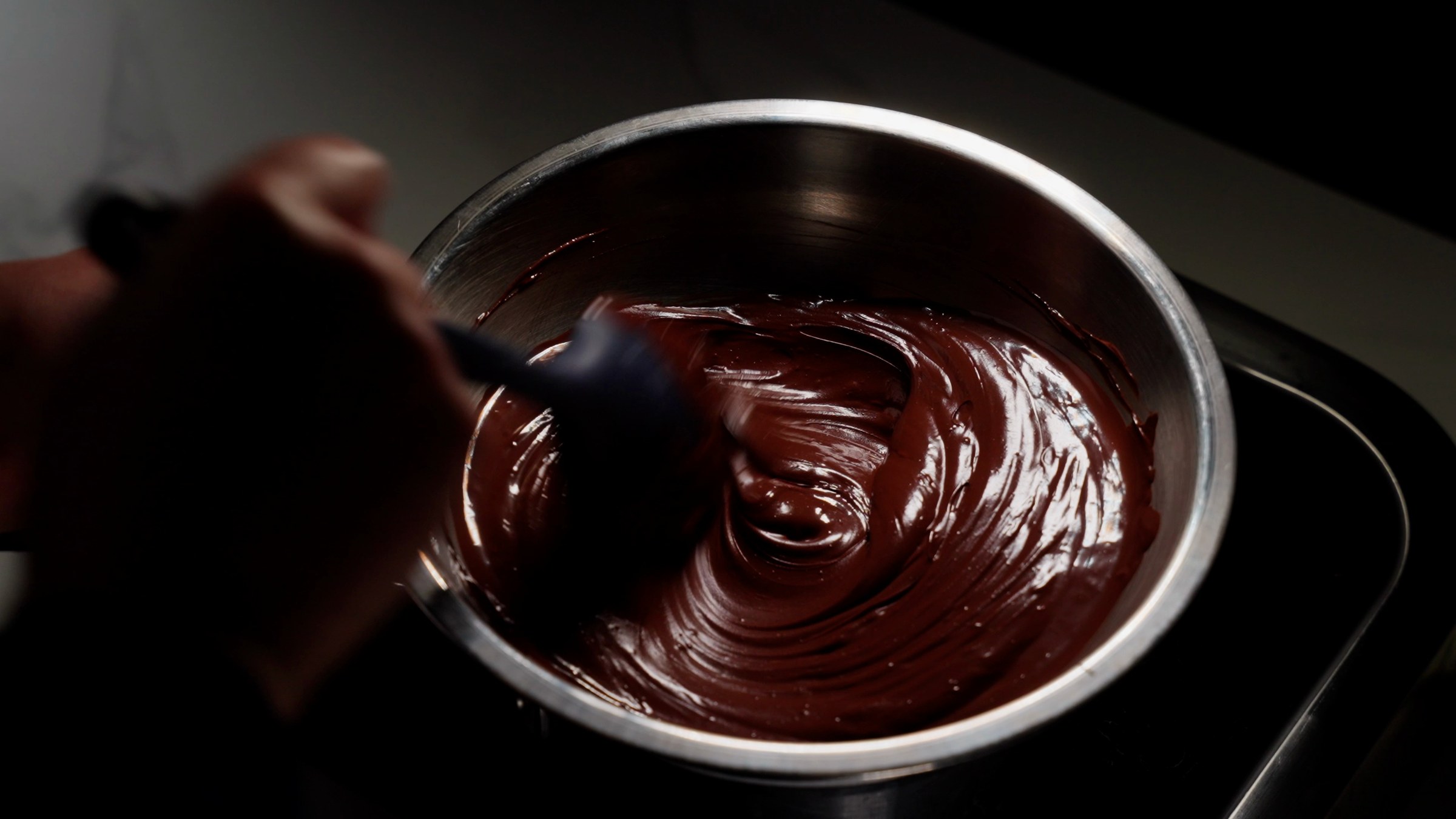 Chocolate ganache being stirred in a steel bowl