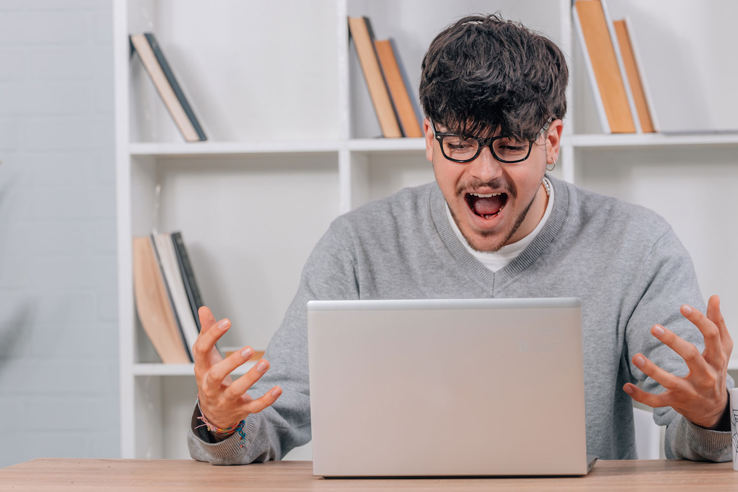 Man sitting at a desk looking frustrated while using a laptop