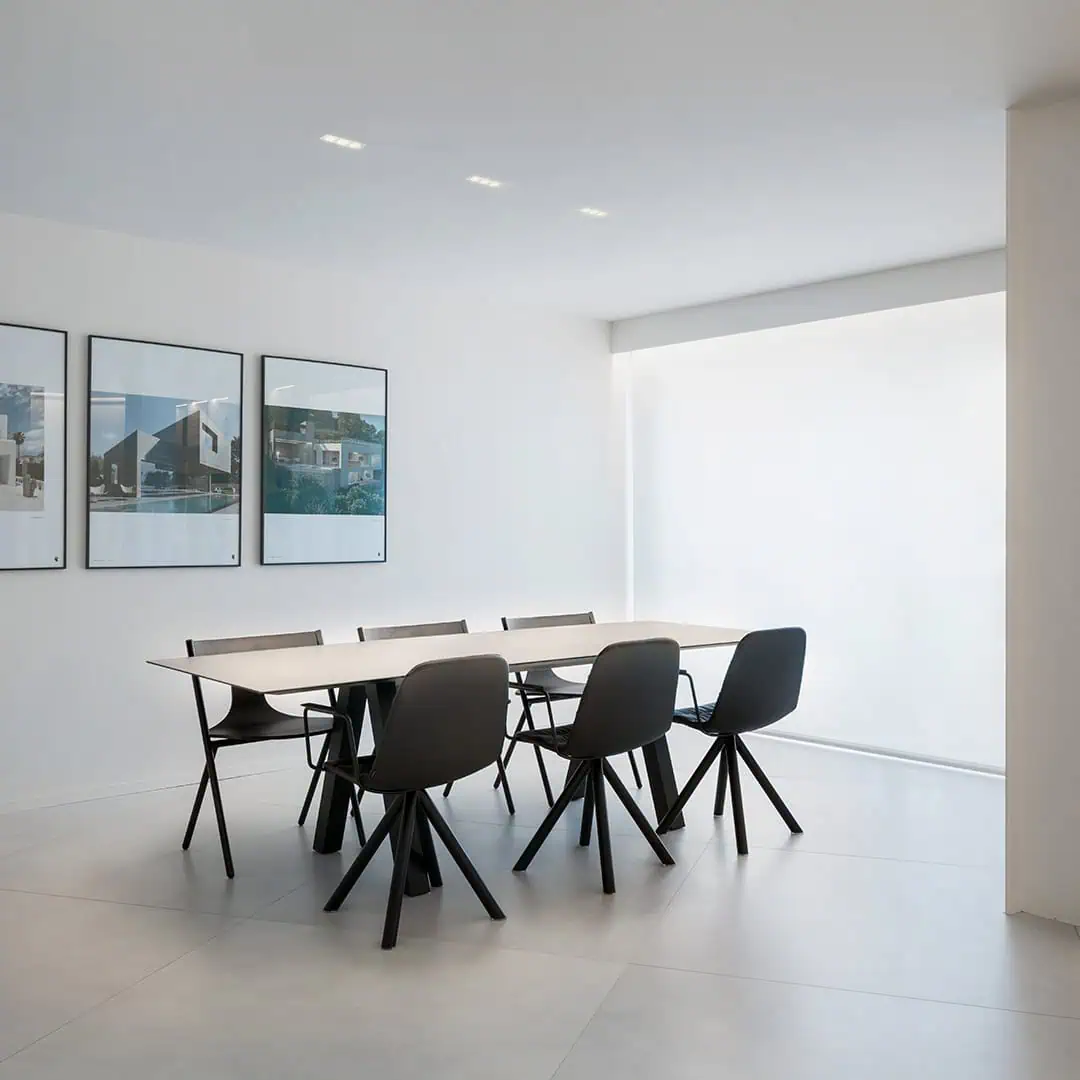 A sleek white dining room featuring modern black chairs around a minimalist table.