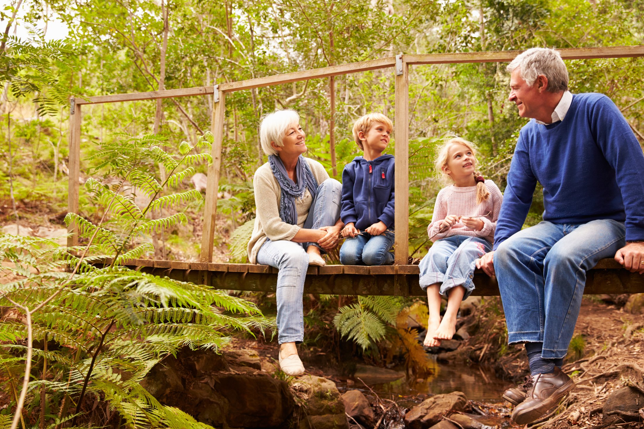 An elderly couple with their grandchildren sitting on a wooden bridge on a greeny environment