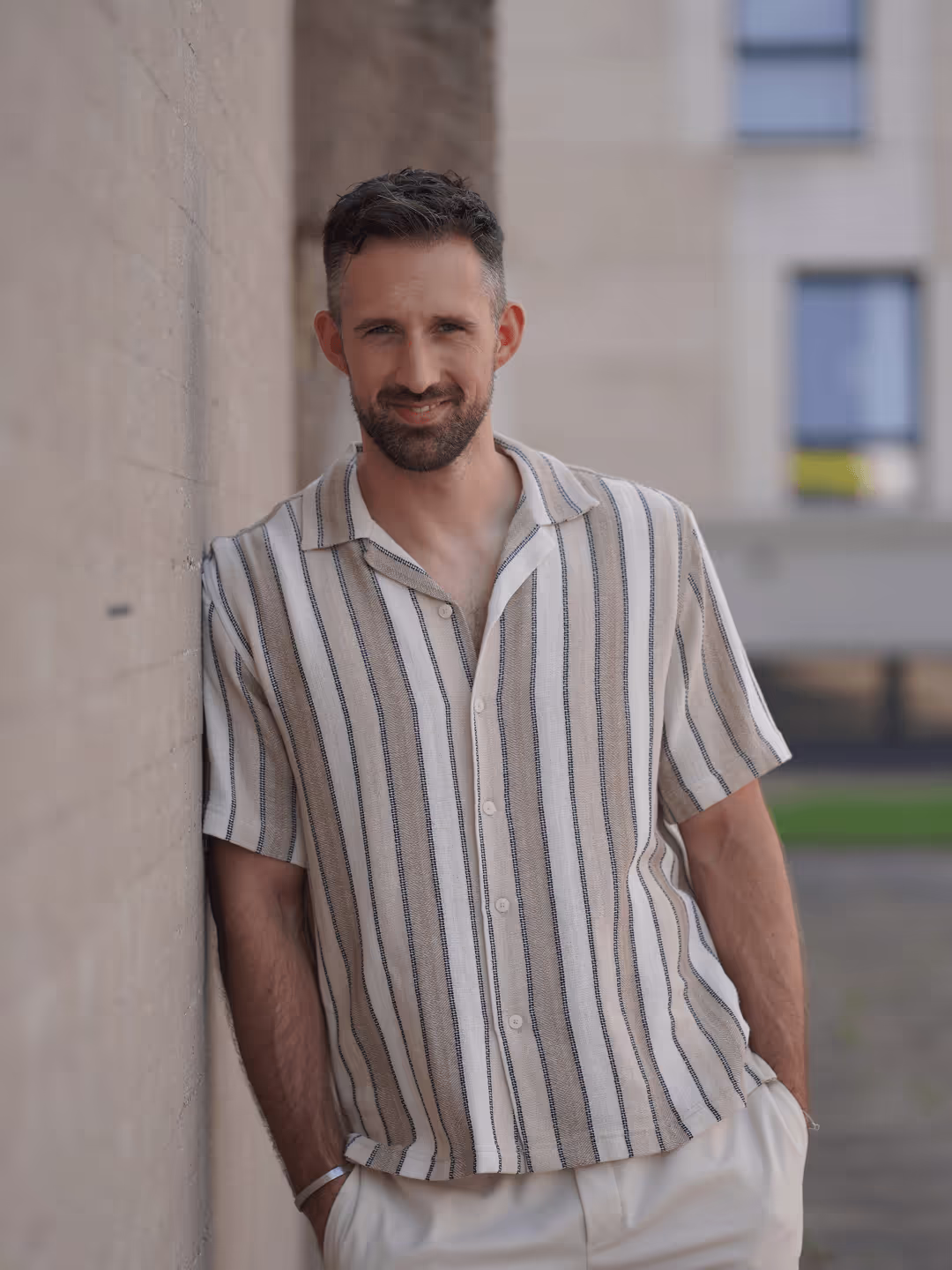 Mann mit weiß beigem Hemd an einer Wand angelehnt