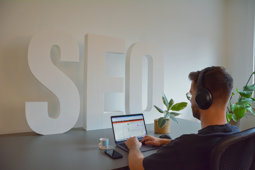Focused professional working at an SEO agency, seated at a modern office desk. He is wearing headphones to stay concentrated, with large 'SEO' letters in the background emphasizing the digital environment. On the desk, there is a cup of espresso, a mobile phone, and a small plant, adding a touch of greenery to the workspace.