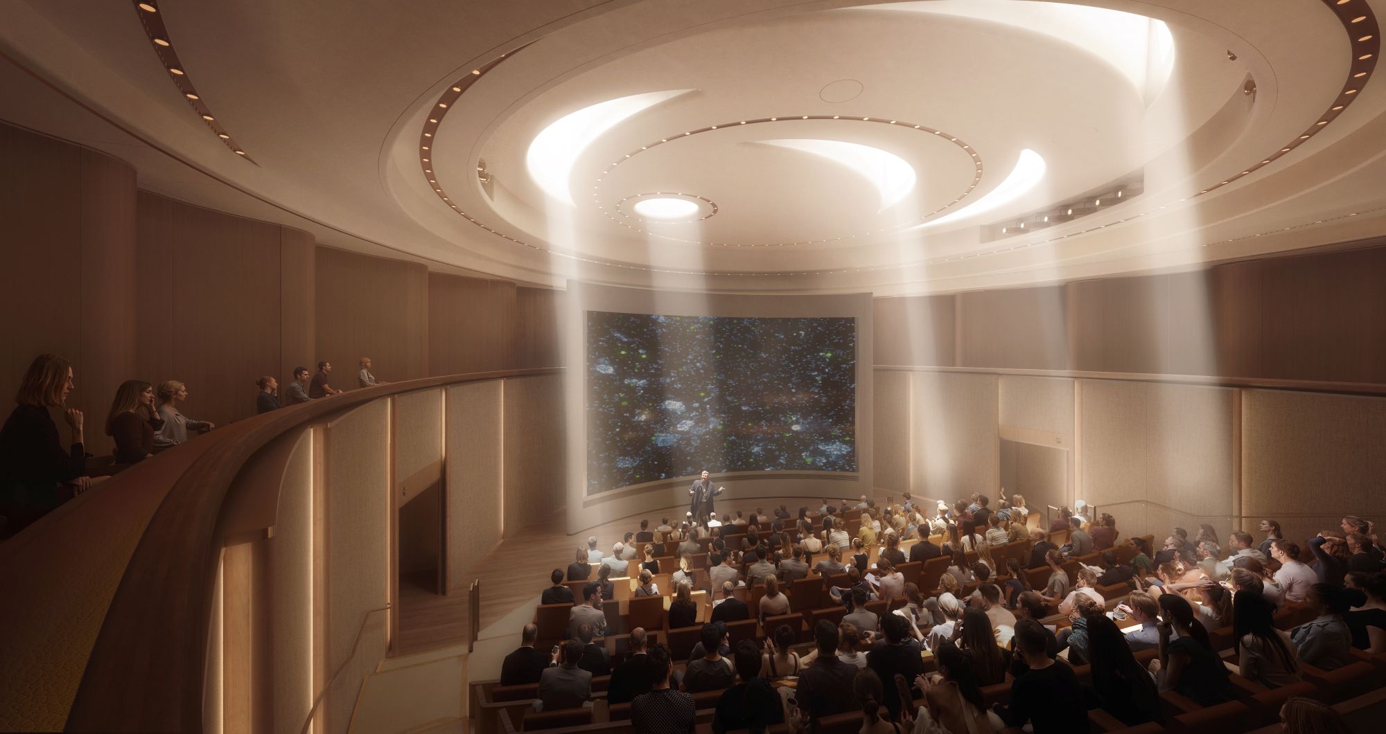 A speaker stands center stage in a sunlit, circular wood-paneled auditorium with tiered seating beneath concentric skylights, addressing a full audience at the Ellison Institute of Technology.