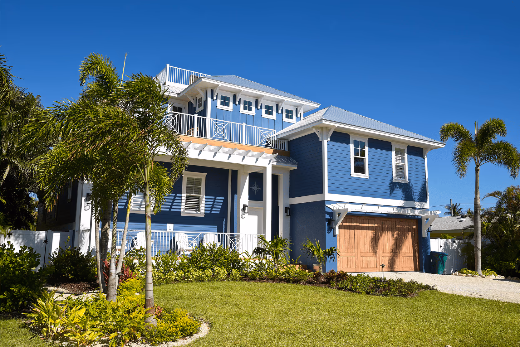 A modern two-story blue house with white trim, featuring a balcony, lush landscaping, and a palm tree in the front yard, ideal for a cost segregation study.