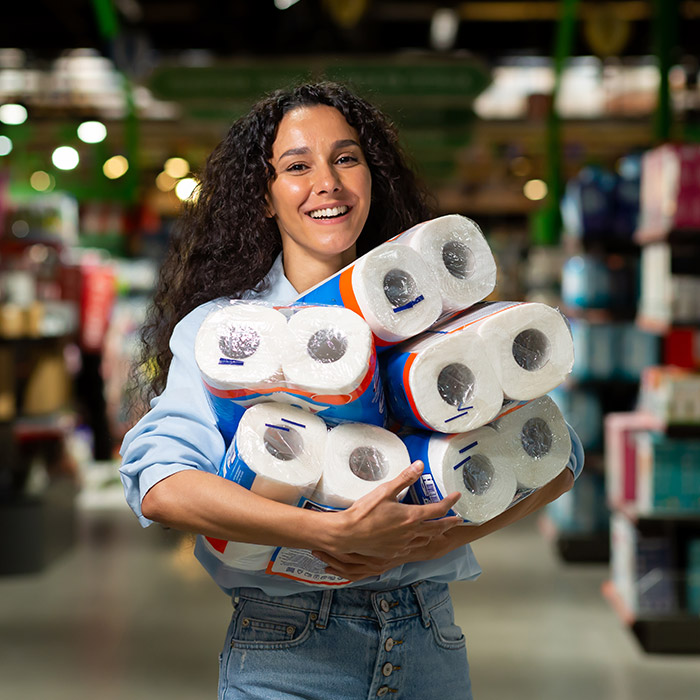 Smiling woman holding bulk packs of paper towels in a grocery store aisle, representing Orderly's rental restock service

