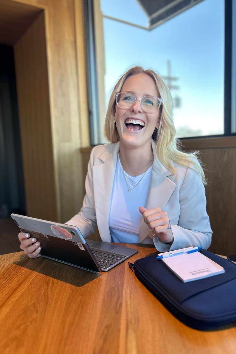 Shay, founder of Orderly Services, smiling while working on a tablet at a café table with sunlight streaming in