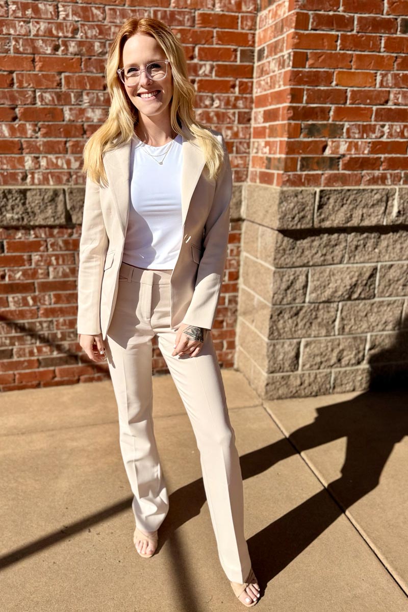 Shay, founder of Orderly Services, standing in sunlight wearing a cream suit in front of a red brick wall