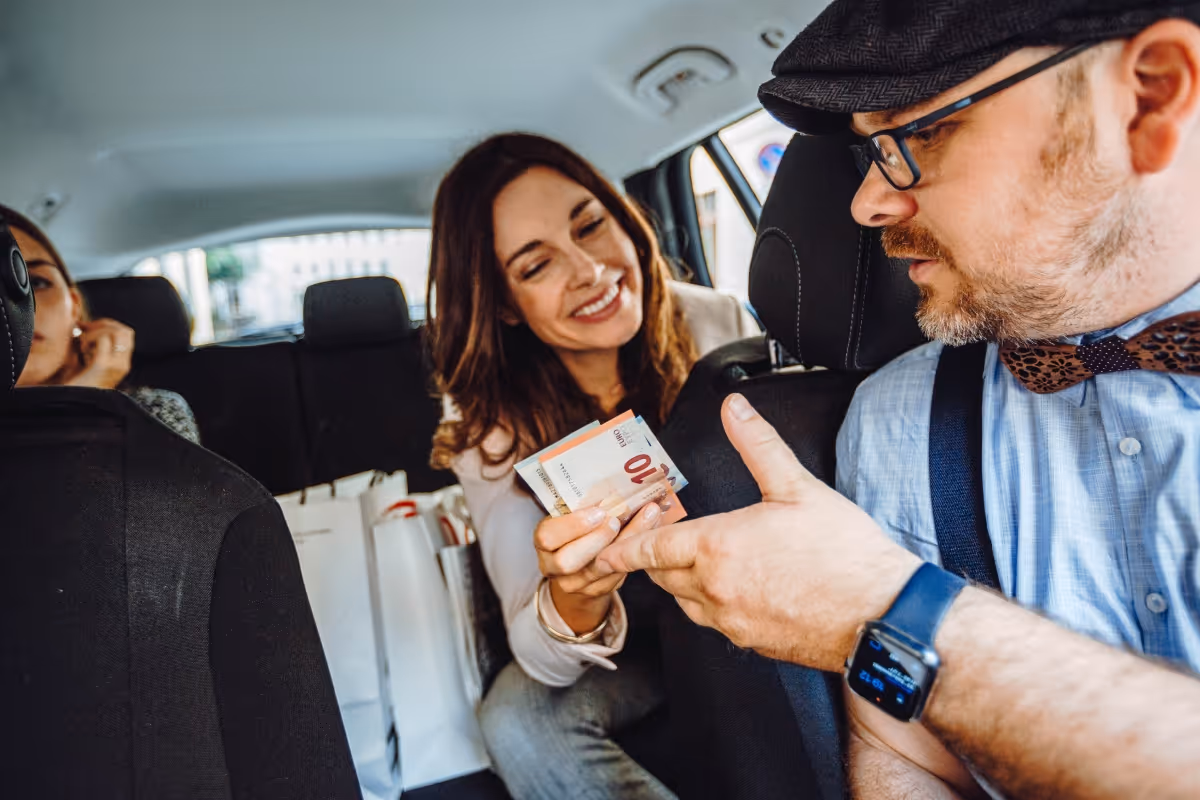 Eine Frau bezahlt den Taxifahrer mit einem 10-Euro-Schein im Auto.

