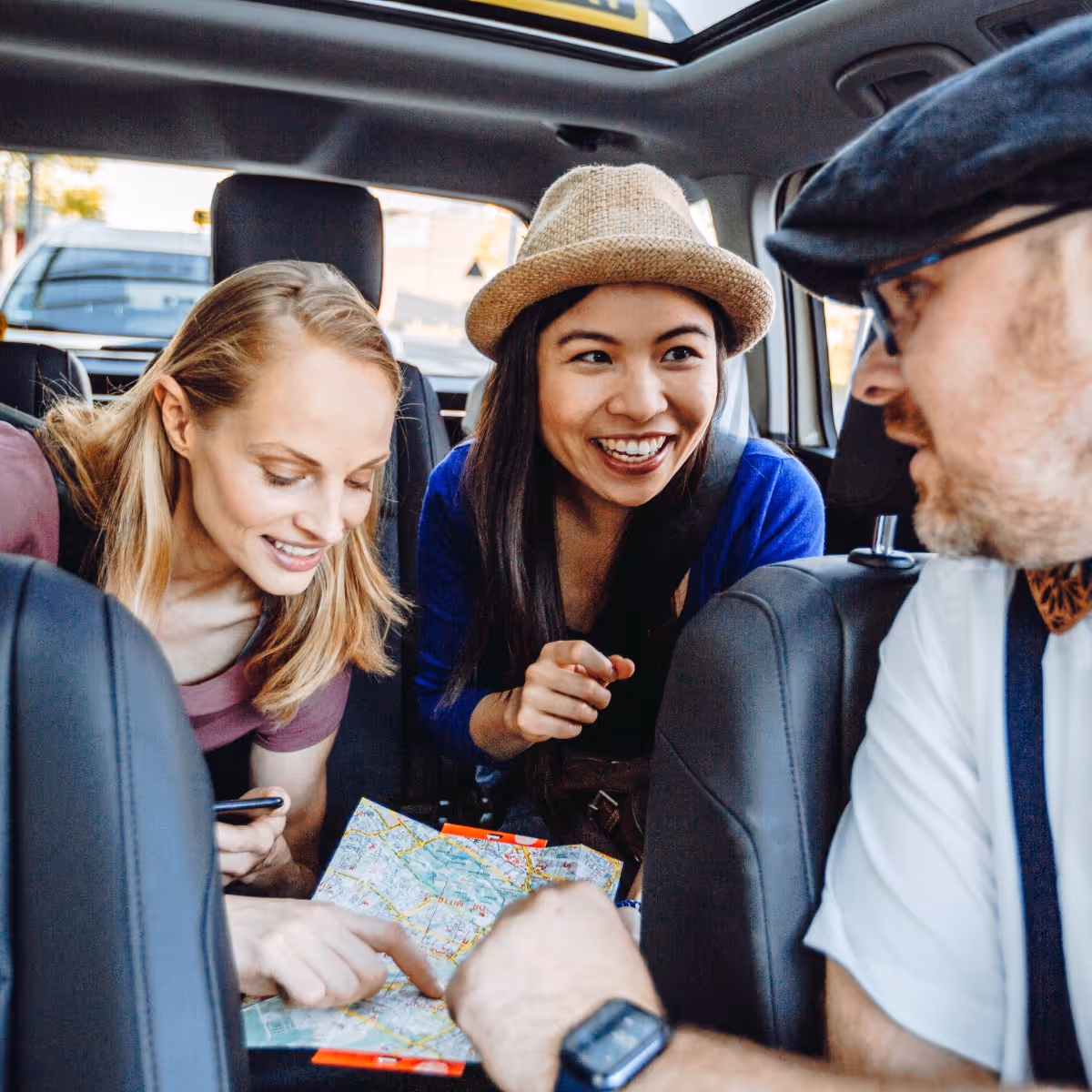 Ein Taxifahrer schaut mit einem Stadtplan auf seine beiden Fahrgäste, die ebenfalls einen Blick auf die Karte werfen.