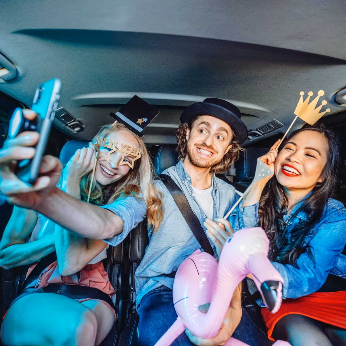 Drei Freunde machen im Taxi ein Selfie mit Party-Accessoires.
