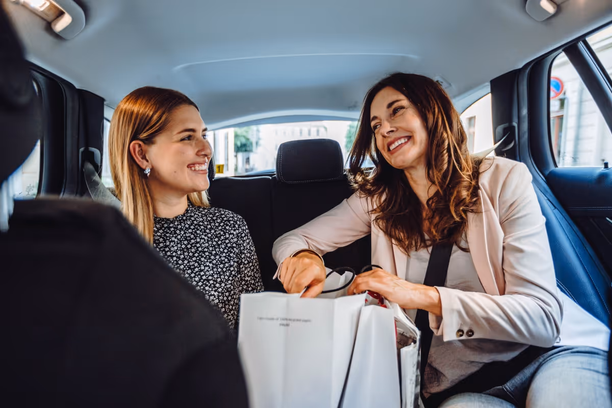 Zwei Frauen sitzen lachend auf der Rückbank eines Taxis.
