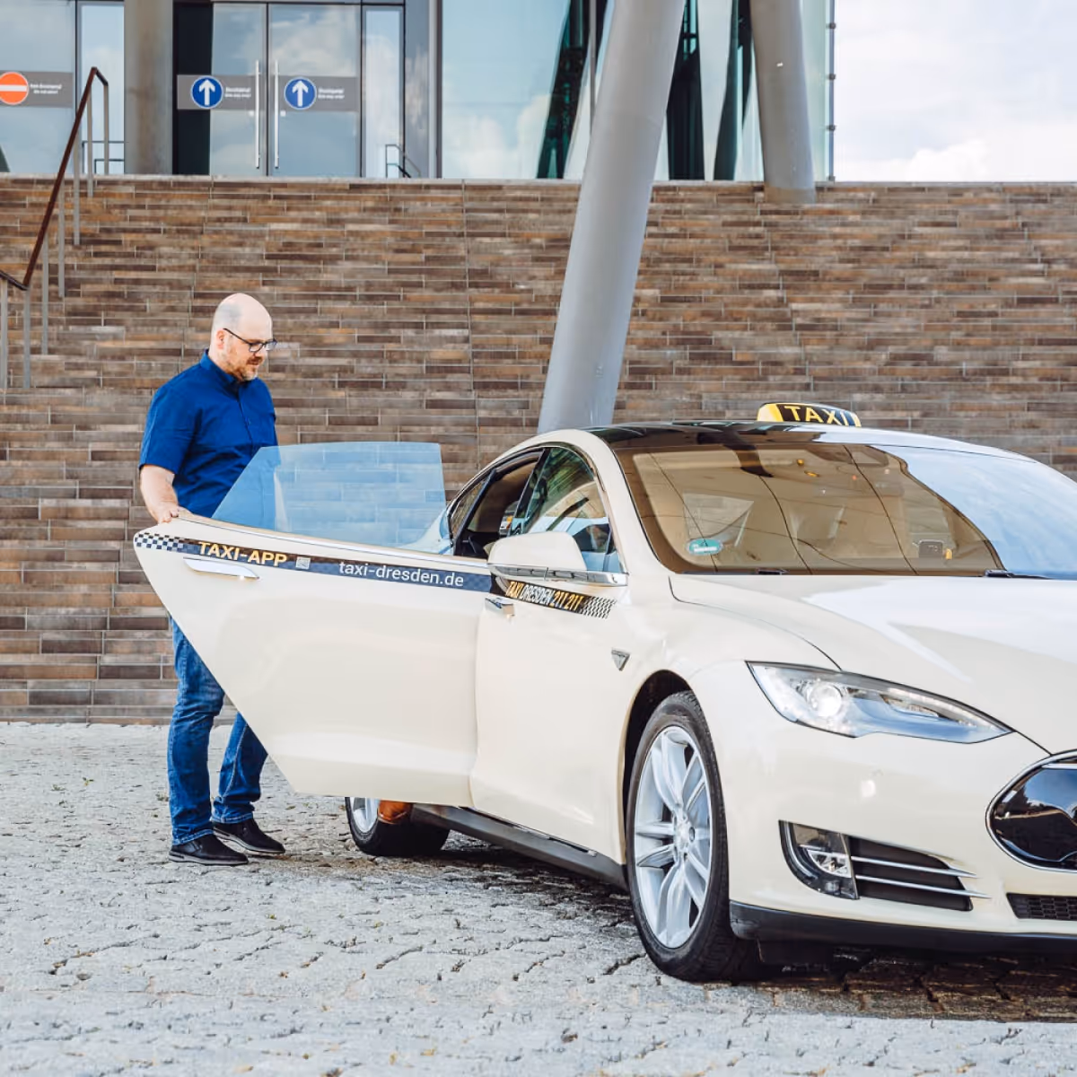 Ein Taxifahrer steht an einem Taxi und öffnet die Fahrertür.