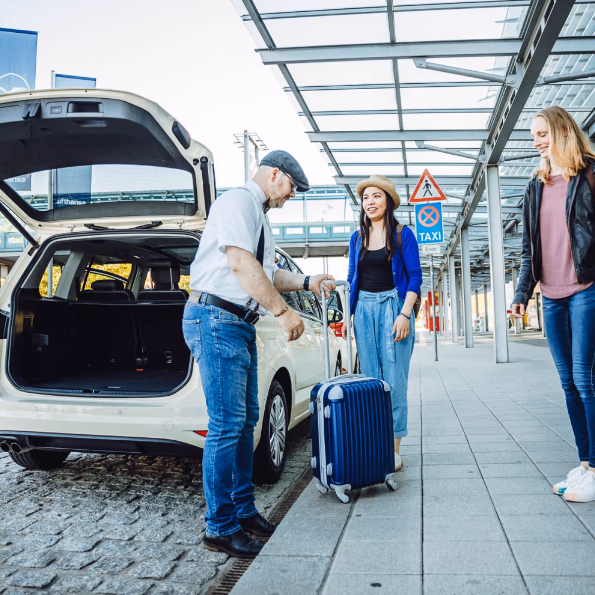 Ein Taxifahrer hilft einer Frau am Flughafen, ihren Koffer in den Kofferraum zu legen.