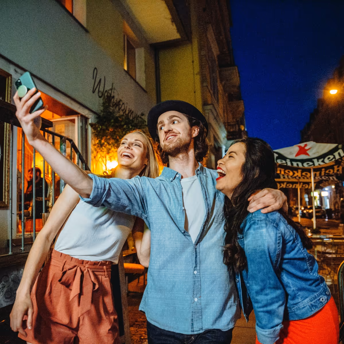 Drei junge, fröhliche Freunde machen nachts ein Selfie auf der Straße.