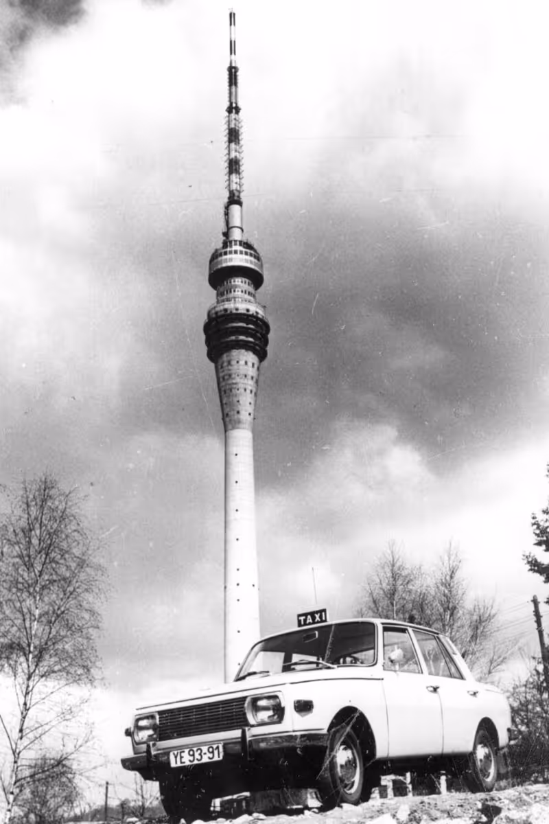 Ein Schwarz-Weiß-Foto eines Taxis aus den 1980er Jahren vor dem Fernsehturm in Dresden.