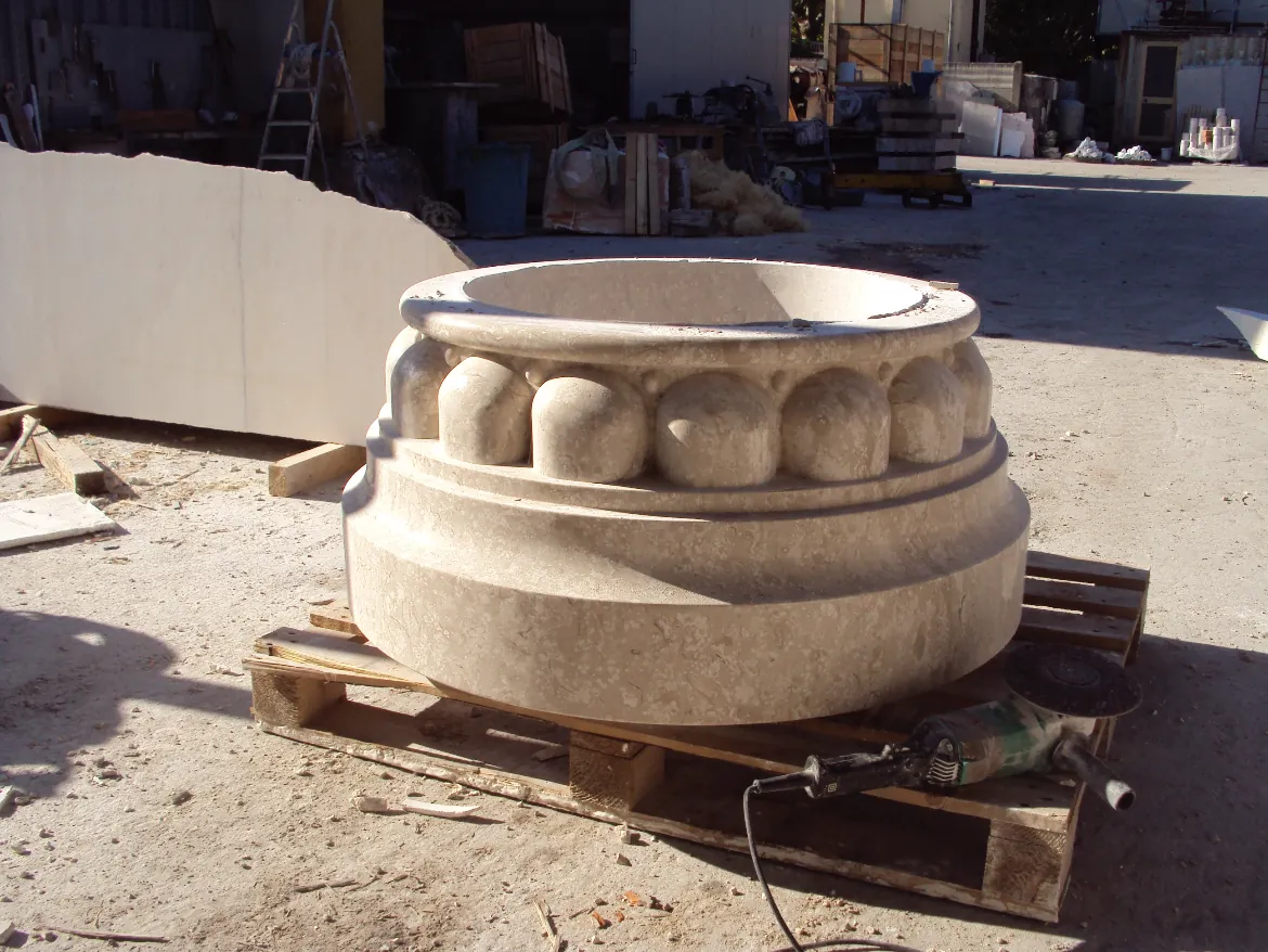 Large decorative stone capital with egg-and-dart design resting on a wooden pallet outdoors.