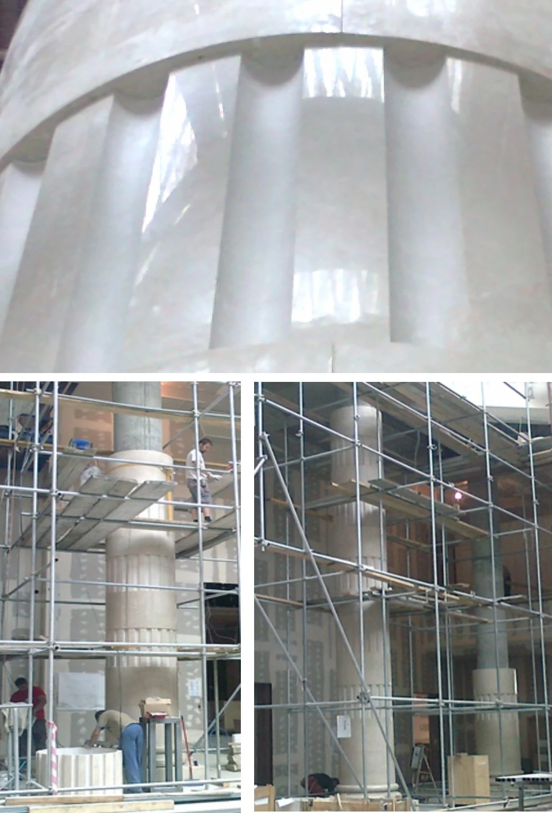 Construction workers installing large stone columns inside a building with metal scaffolding around them.