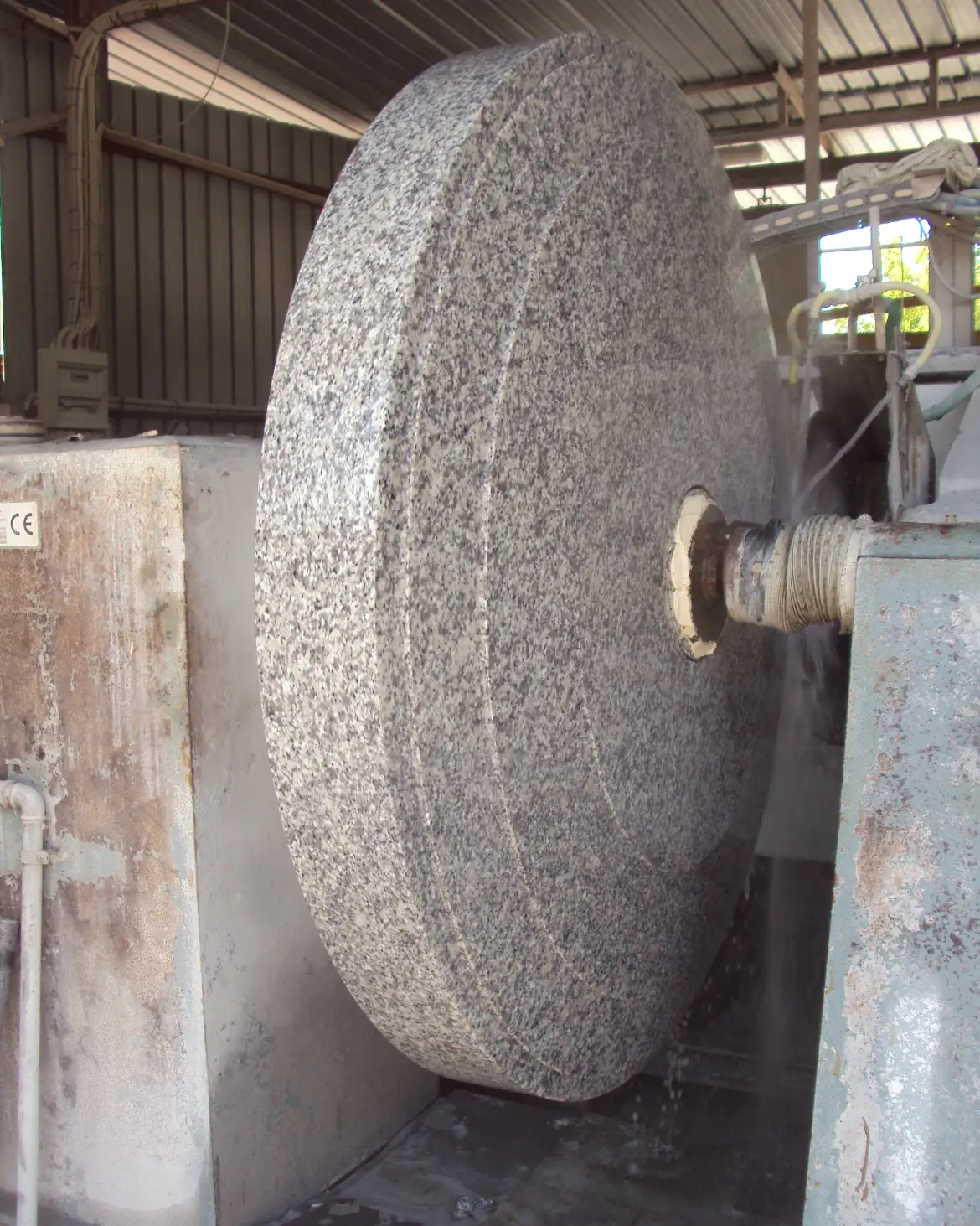 Large circular granite stone being cut or polished by industrial machinery in a workshop.