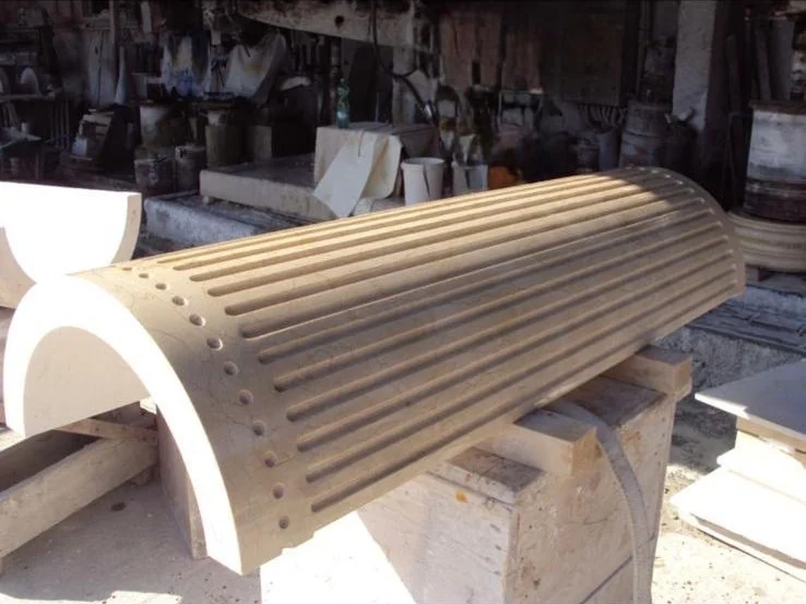 A curved architectural column segment with vertical grooves resting on wooden supports in a workshop.