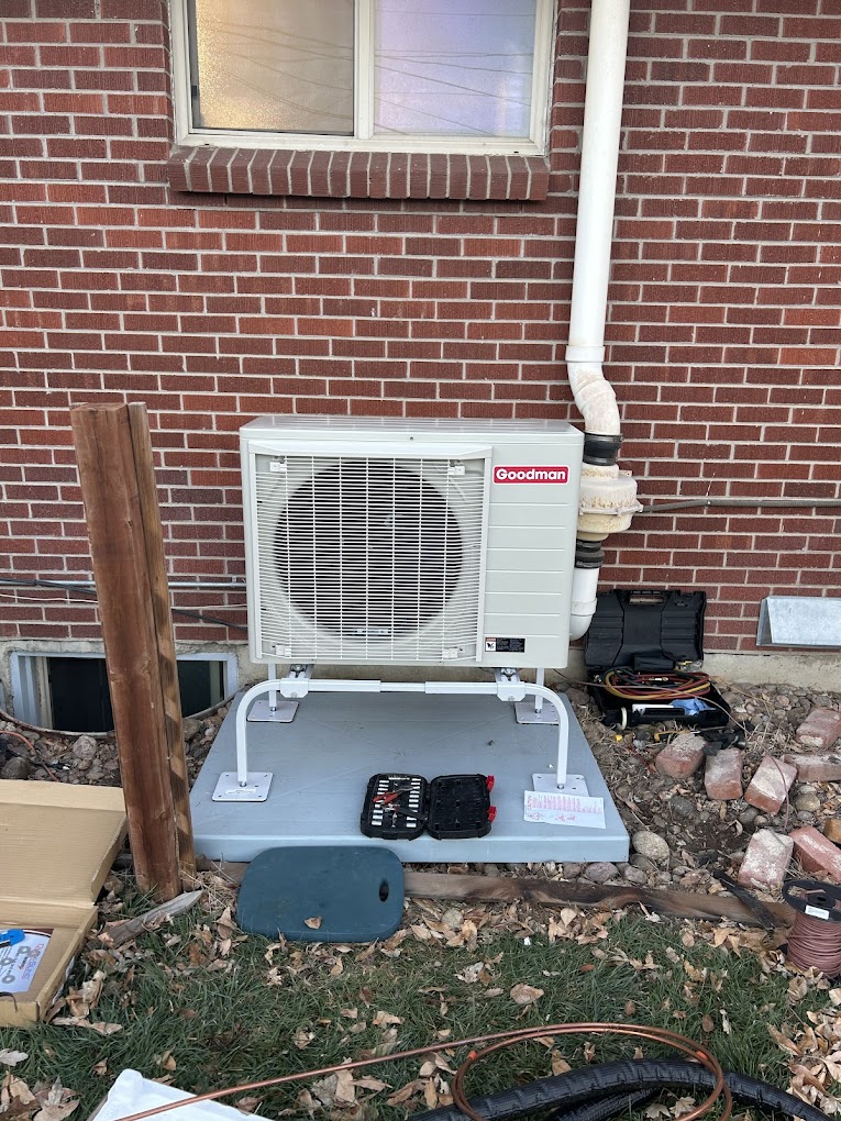 Goodman HVAC unit installed outside a brick house, with tools and equipment nearby, illustrating HVAC repair services by Colorado Bear Heating & Air in Castle Rock, CO.