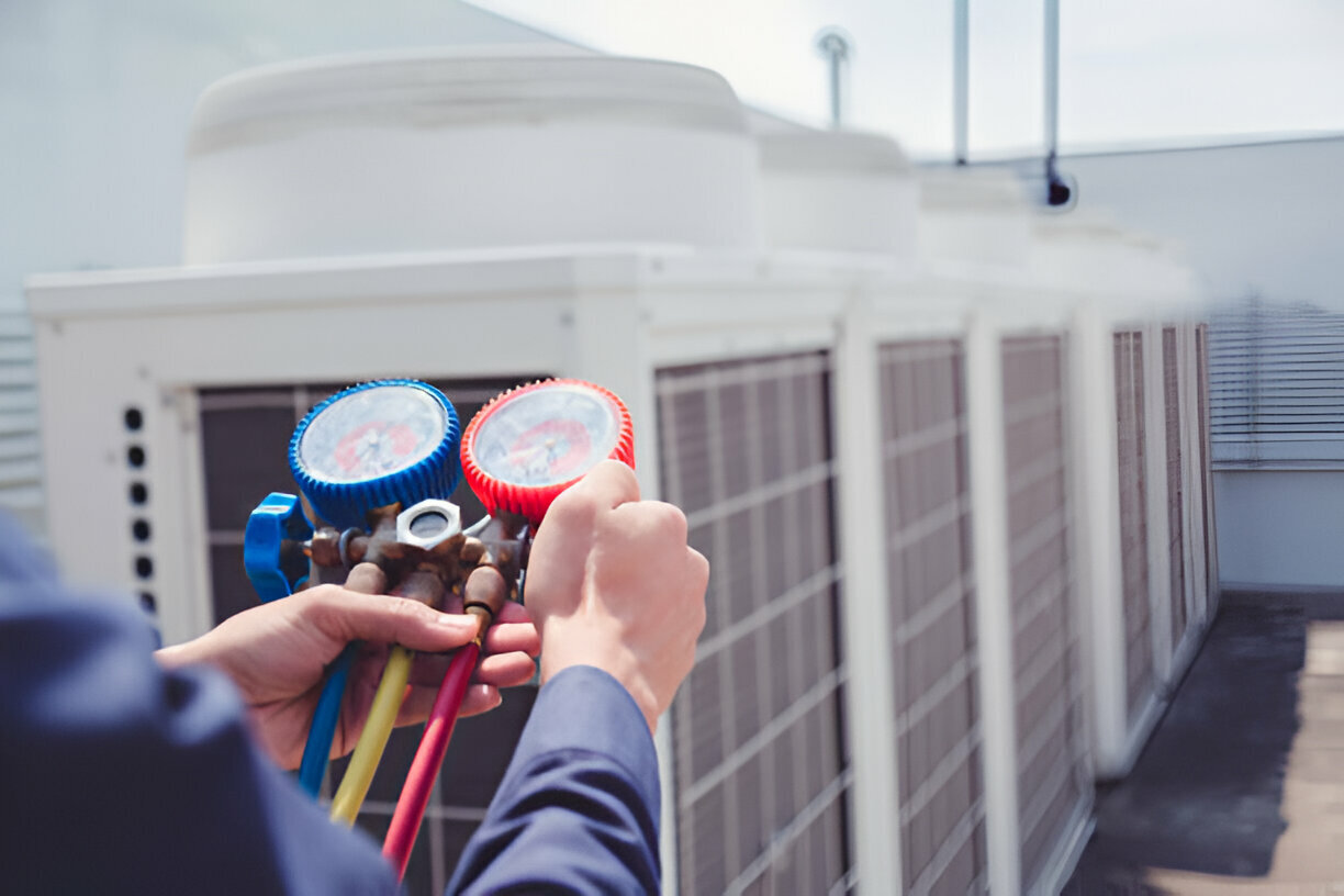 Technician holding AC manifold gauge set in front of outdoor air conditioning units, illustrating expert AC repair services in Castle Rock, CO.