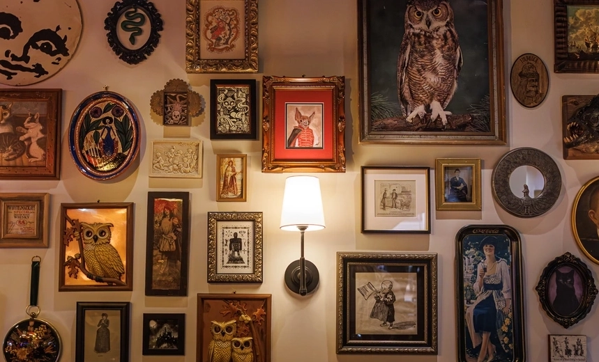 Gallery wall of mismatched vintage frames with images of owls, snakes, portraits, and other occult symbols