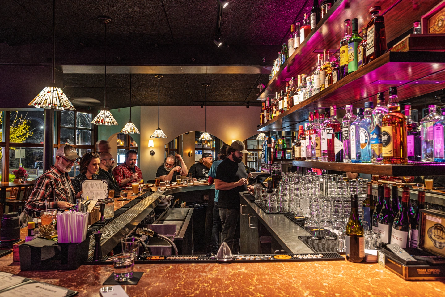 Patrons sitting at the bar while the bartender makes drinks