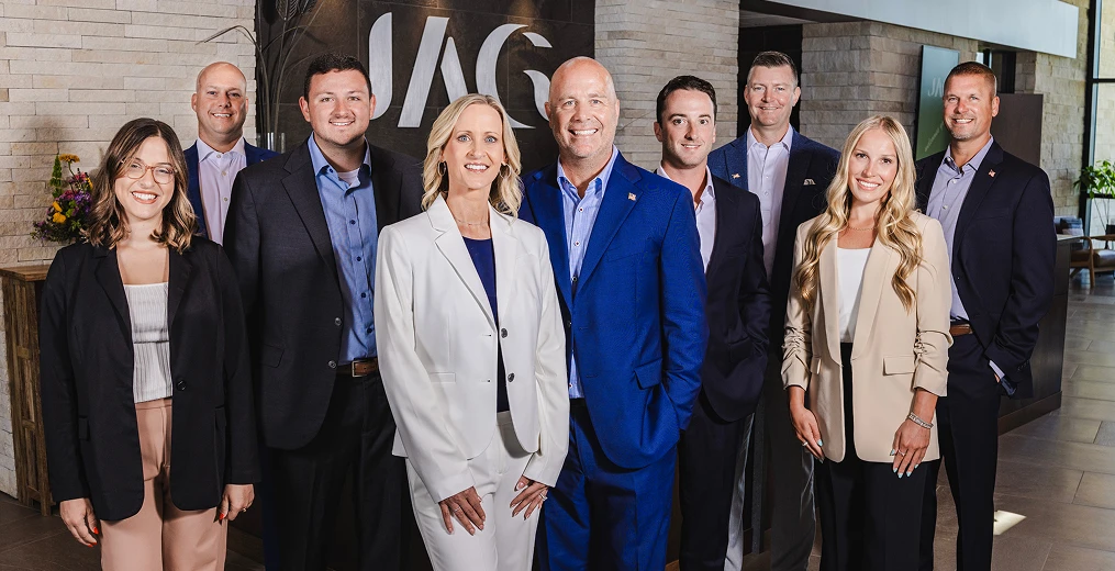 Nine team members from Jones Advisory Group standing inside their office in front of their logo sign, smiling.