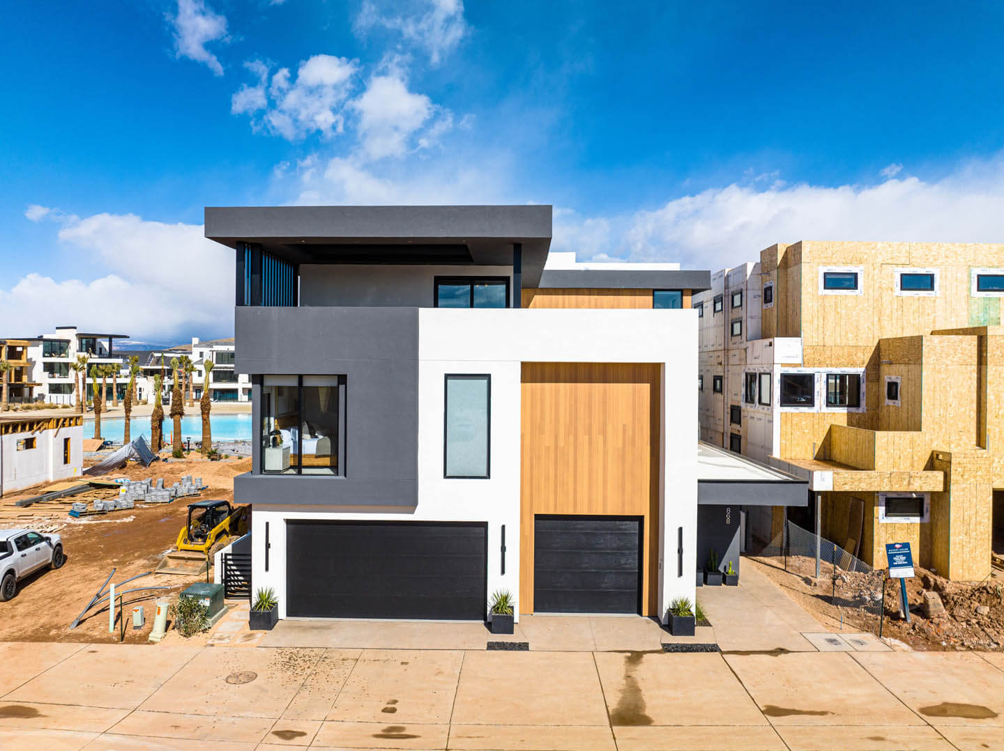 Modern house exterior at night with illuminated large glass windows, a swimming pool, and three white lounge chairs on the poolside patio.