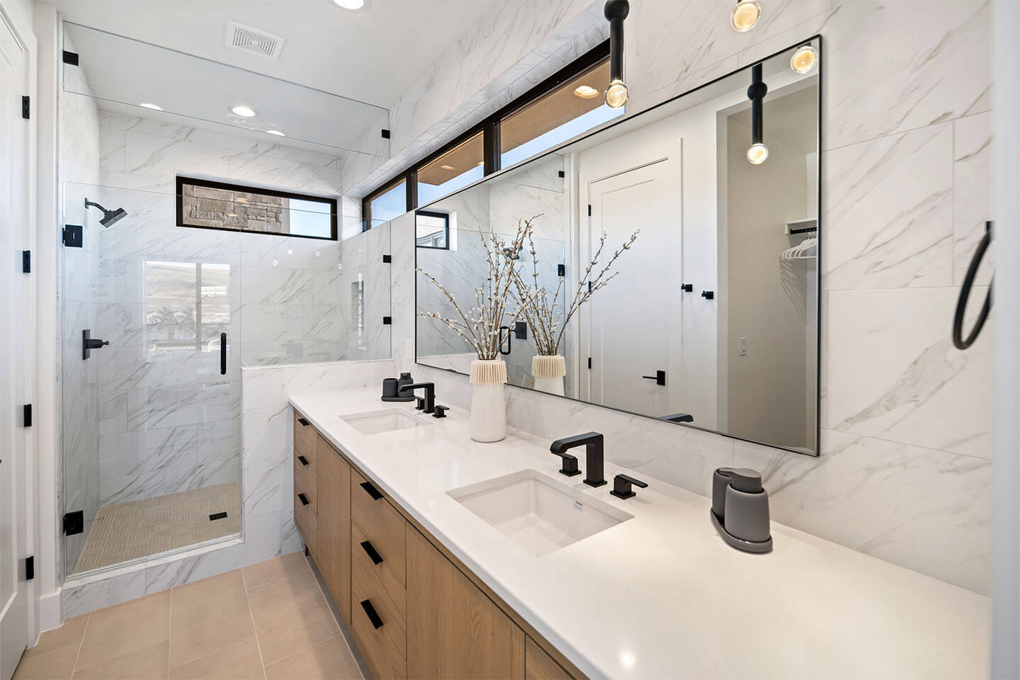 Modern bathroom with double sinks, black fixtures, large mirror, wooden cabinets, and a glass-enclosed shower with marble walls.