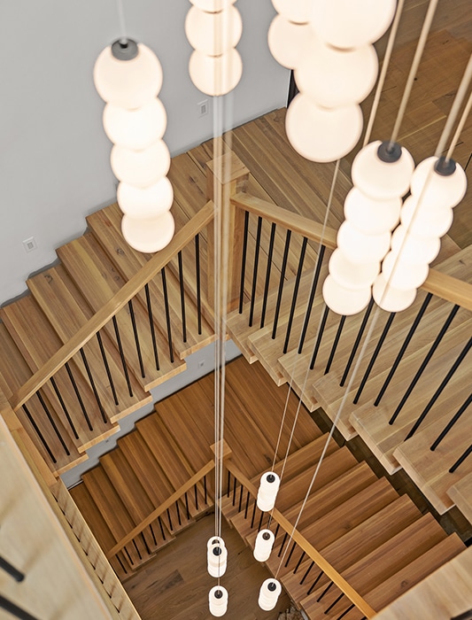 Overhead view of a multi-story wood staircase with black metal balusters and a cascading cluster of globe pendant lights