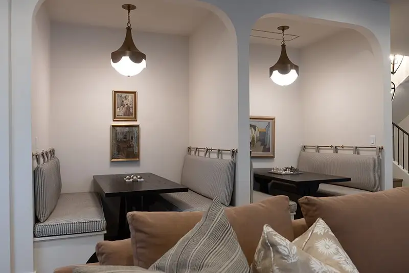 Interior dining nook with arched alcoves, upholstered banquette seating, dark wood tables, and bronze pendant lights