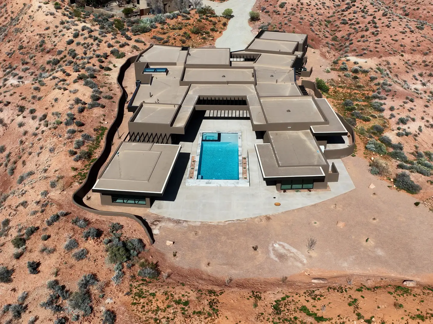 Aerial view of a sprawling flat-roof custom home with courtyard pool built into red desert terrain near St. George, Utah.