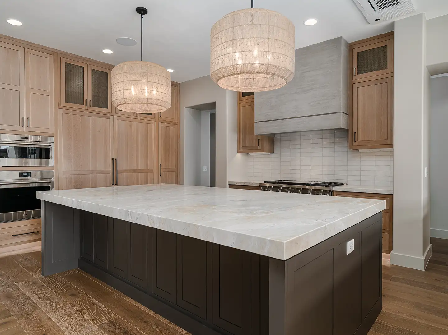Kitchen with dark-base marble island, natural oak cabinetry, woven drum pendant lights, and stainless steel appliances.