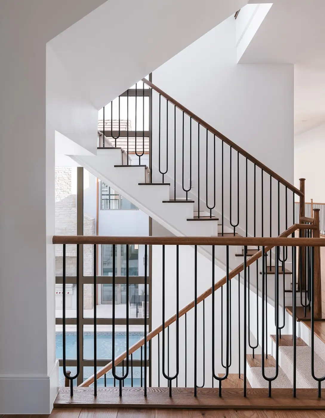 Bright interior staircase with white painted steps, oak wood handrail, black iron pin balusters, and an overhead skylight.
