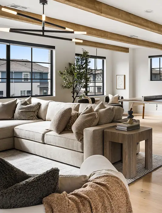 Open-concept game room with exposed wood ceiling beams, ping pong table, neutral sofa, and a round black pedestal dining table