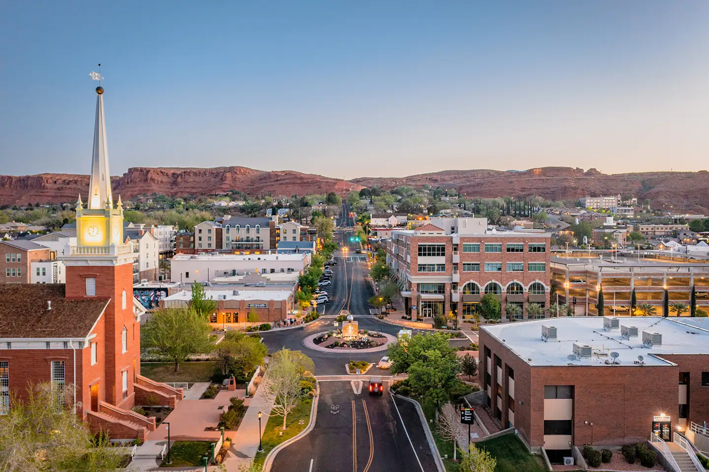 Aerial view of downtown St. George, Utah at dusk featuring the historic tabernacle steeple and distant red rock ridges.