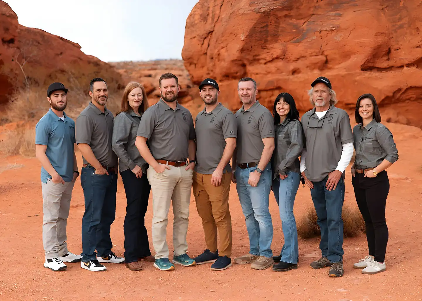 Smiling home builder team in branded grey polos posed together in front of vivid red sandstone canyon walls.