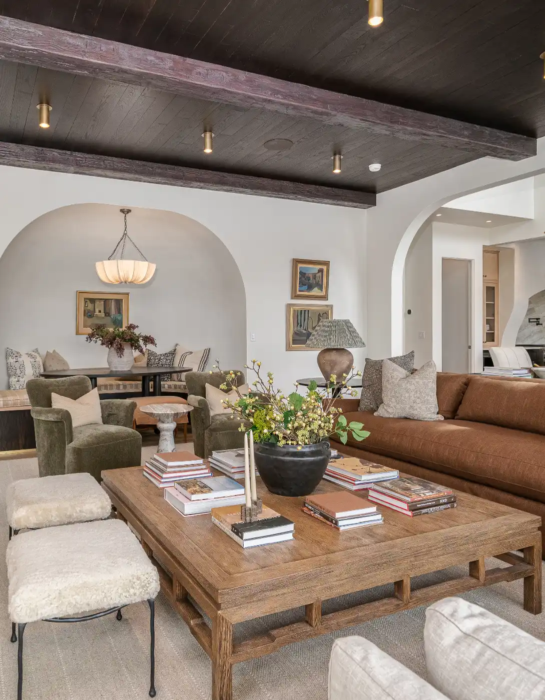 Cozy living room with exposed dark ceiling beams, arched openings, built-in shelves, and a sofa and chairs around a wood coffee table