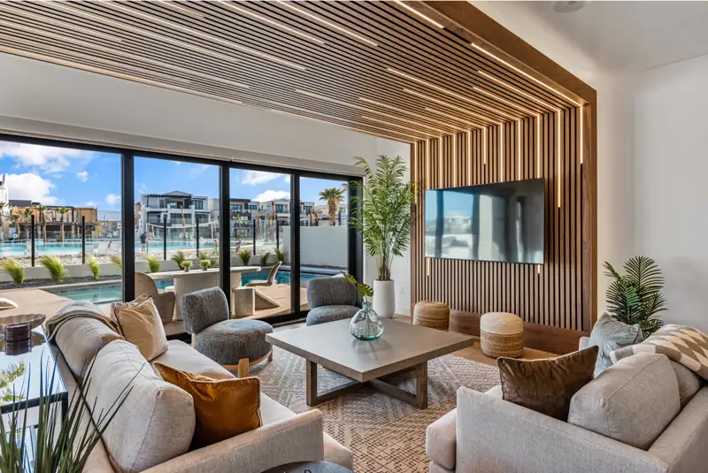 Living room with wood-slat ceiling and accent wall, wall-mounted TV, sofas, and sliding doors opening to a pool and community view.