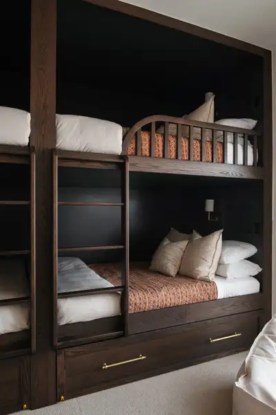 Bedroom with built-in dark-wood bunk beds, ladders, white and patterned bedding, and a storage drawer below.
