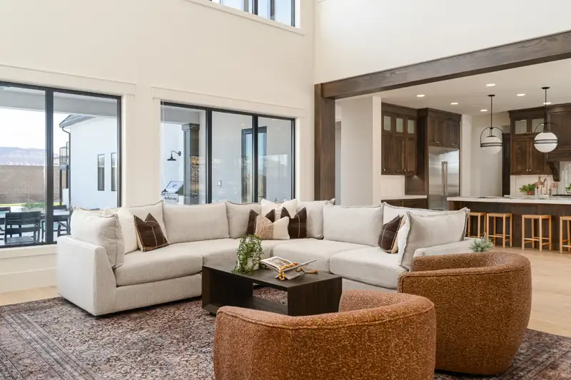 Open-concept living room with a white sectional sofa, round swivel chairs, large windows, and a view into the kitchen.