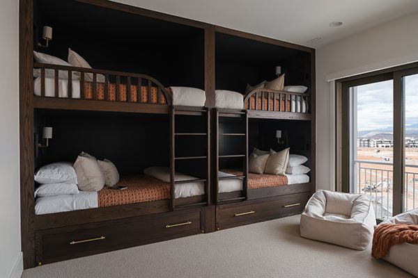 Bedroom with four dark wood built-in bunk beds, white bedding, storage drawers, and a sliding door to a balcony.