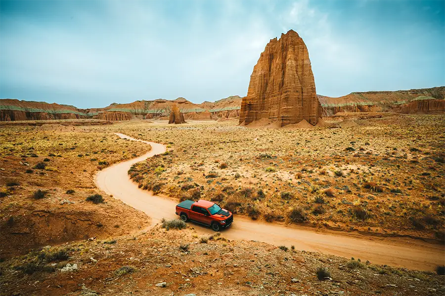 Red pickup truck on a winding dirt road through the desert with a tall sandstone formation behind